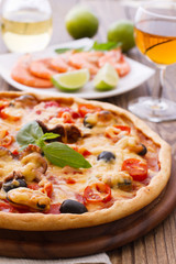 Big tasty pizza with seafood, tomatoes, wine on wooden table