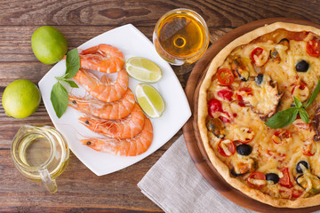 Big tasty pizza with seafood, tomatoes, wine on wooden table