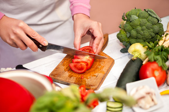 Cutting tomato on slices, woman preparing vegetable in the kitch
