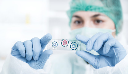 woman in a laboratory microscope with microscope slide in hand.