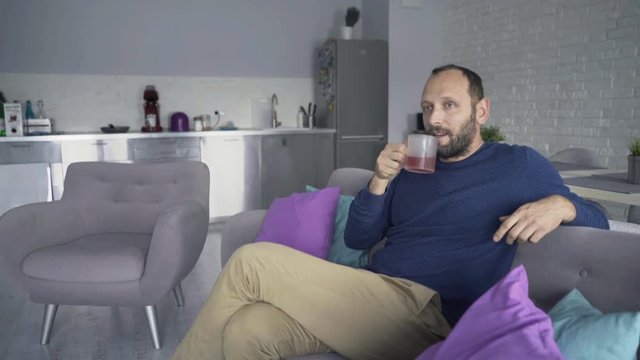 Young, happy man relaxing and drinking coffee on the sofa, 4K
