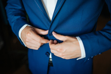 Wedding preparation. Groom buttoning his blue jacket before wedding. Closeup of man buttons his jacket. Selective focus.