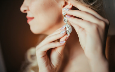 Wedding preparation. Beautiful, happy bride dresses earrings before wedding. Wedding accessories,...