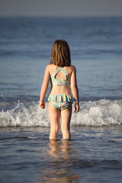 young girl wading in the ocean watching an oncoming wave move towards her