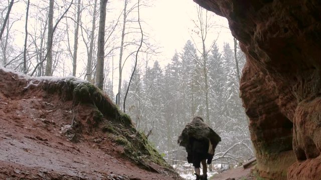 Prehistoric caveman goes outside from his cave on a background of winter forest