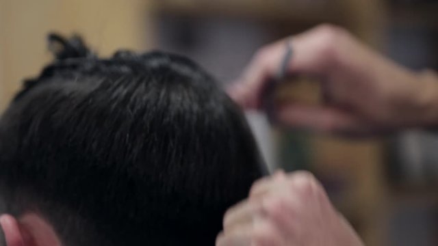 Barber making haircut of attractive bearded man in barbershop.