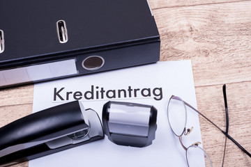 Kreditantrag mit Ordner und Brille auf Holztisch