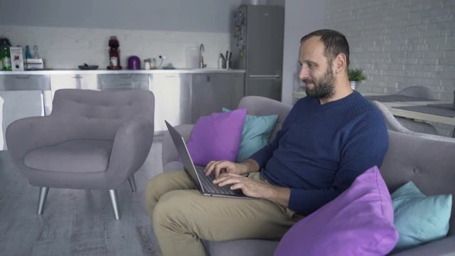 Young, handsome man using laptop sitting on sofa, 4K
