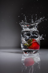 strawberry splash into water glas on grey black background