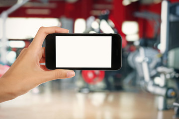 Female hand with smartphone against blurred gym interior background