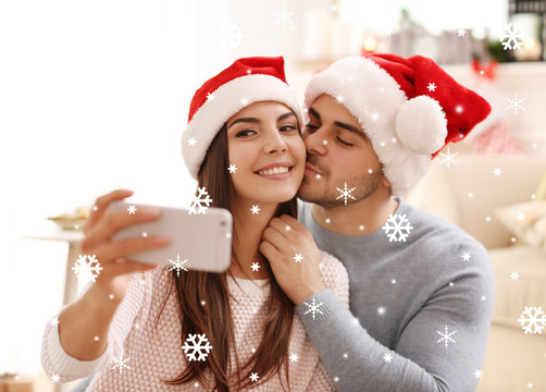 Happy young couple taking selfie at home. Snowy effect. Christmas celebration concept.