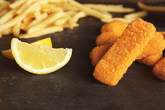 Tasty fish nuggets with fries and lemon on table