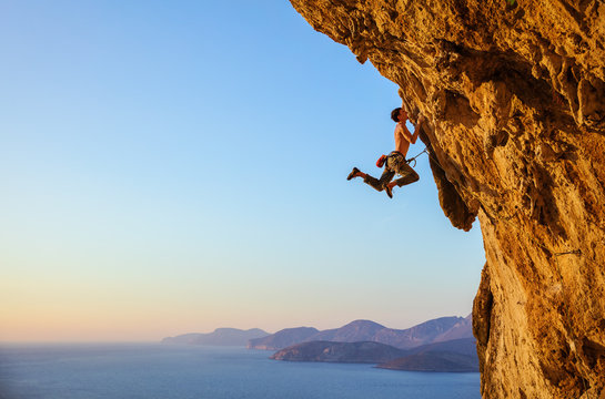 Rock climber jumping on handholds while climbing overhanging cliff