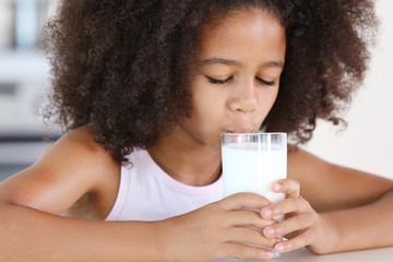 Curly African-American girl drinking milk for a breakfast in the kitchen