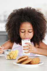 Pretty African-American girl drinking milk with pleasure at breakfast in the kitchen