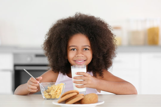 Pretty African-American girl drinking milk with pleasure at breakfast in the kitchen