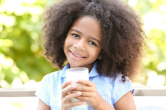 Pretty African-American girl with a glass of milk in the garden