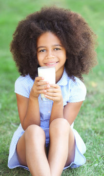 Pretty African-American girl drinking milk and sitting on the lawn
