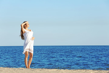 Fototapeta na wymiar Young pregnant woman in white dress standing on the beach