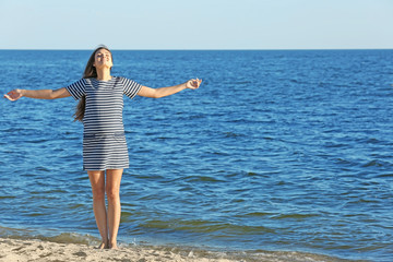 Fototapeta na wymiar Beautiful pregnant woman in striped dress standing on the beach