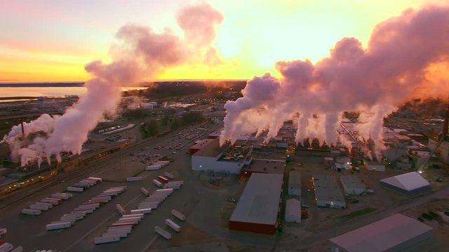 Many industrial smokestacks billowing smoke into red predawn sky.
