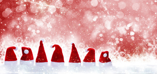Weihnachtsmützen im Schnee vor rotem Bokeh