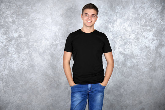 Handsome young man in blank black t-shirt standing against grey textured wall