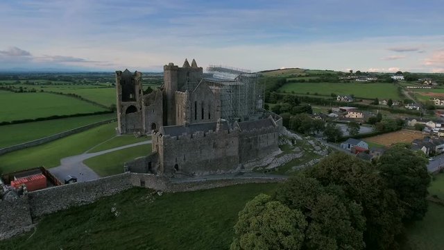 Amazing aerial shot of the Rock of Cashel with lots of trees surrounding the hill and the green fields in Ireland