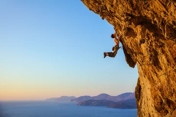 Fototapeten Rock climber jumping on handholds while climbing overhanging cliff © Andrey Bandurenko