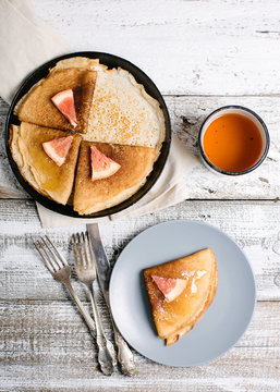 Breakfast of pancakes in a frying pan and on the plate with honey and grapefruit and tea in a cup
