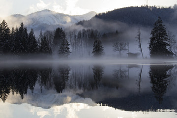 Lake Erlaufsee in Austria in Winter with fog, clouds and sun with nice reflection