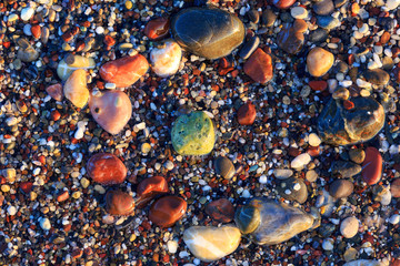 Colored pebbles on the beach, colored pebbles in the water and under water in the glare of the rising sun at dawn, green stone.