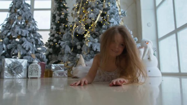 Little happy girl lies near the Christmas tree with gifts