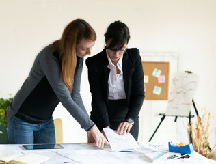 Young redhead female architect and young female investor working in the office. Selective focus and small depth of field.