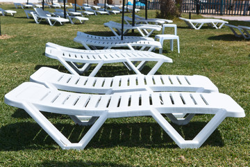 White plastic beach sunbeds are in public area of hotel, nobody