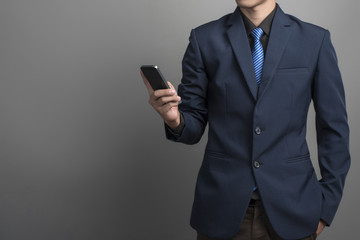Close up of businessman in blue suit using smartphone on gray ba