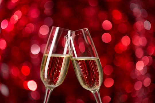 Two glasses of champagne against red background with sparkles. Very shallow depth of field. Selective focus