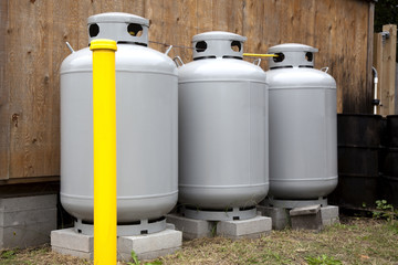 Three gray propane tanks with yellow bollard. Horizontal.