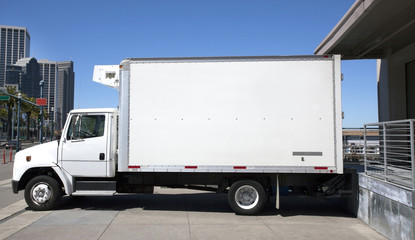 Parked refrigerated truck at loading dock under blue sky. Horizontal.