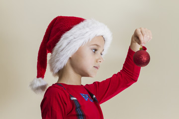 Small child in Santa cap looking at xmas toy near Christmas tree