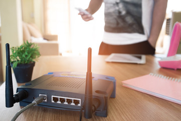 closeup of a wireless router and a young man using a smartphone  on living room at home with a window in the background - obrazy, fototapety, plakaty