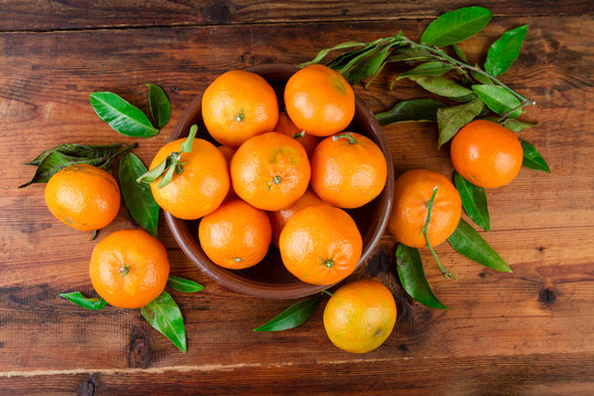 Mandarins tangerines in a ceramic bowl on wooden table. Top view.
