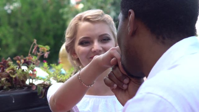 Gallant black man beautiful cares for white girl, kisses the hand of a date in the cafe