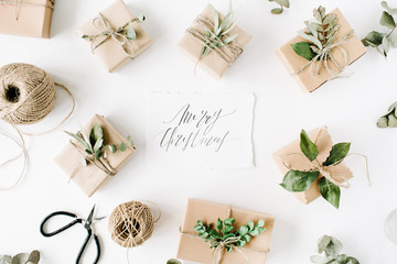 calligraphy words merry christmas and beauty arrangement frame of craft boxes and green branches on white background. flat lay, top view