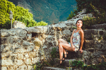 Feminine romantic woman posing in Stari Bar old fortress, Montenegro. Tanned female with long hair, red lips and manicure in white dress flowers. Brunette girl walk around oldest castle