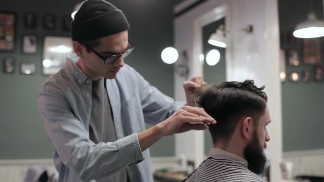 Young handsome barber making haircut of attractive bearded man in barbershop