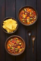 Veganischer Chili aus Kidneybohne, Karotte, Zucchini, Paprika, Mais, Tomate, Zwiebel und Knoblauch, Tortilla Chips an der Seite, fotografiert mit natürlichem Licht