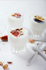 Yogurt in glass cups with nuts,pistachios and fresh figs.Breakfast,Dessert, Pudding on a white background.Food or Healthy diet concept.selective focus.Top view.