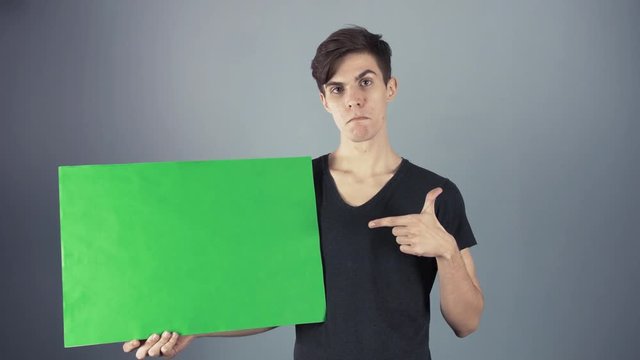 Peased Young man in black shirt holding green key sheet poster gray background