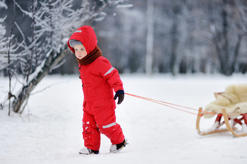 Fototapeta na wymiar Little boy in red winter clothes with toboggan